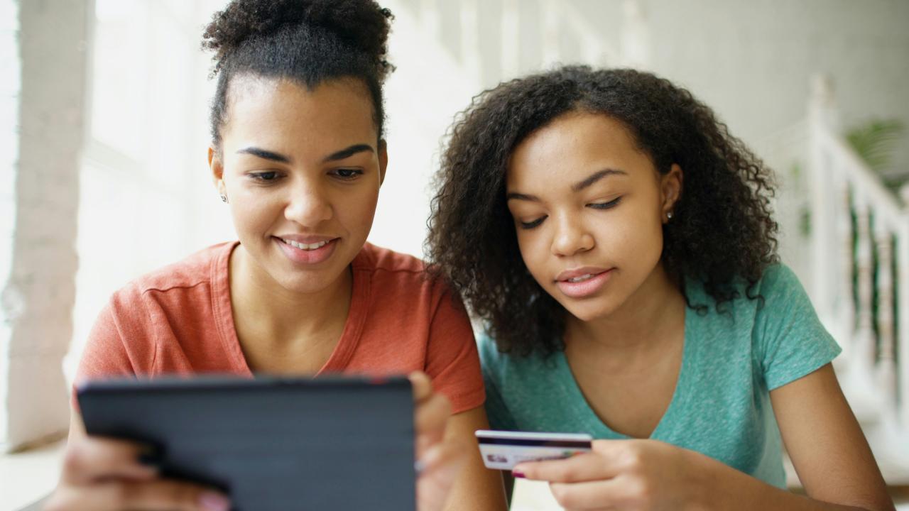 Two young women looking at a tablet with credit card.