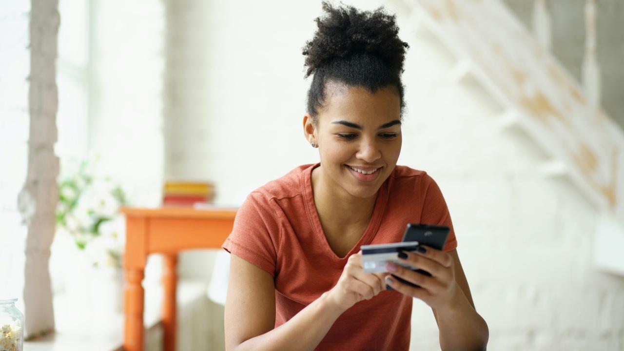 Young woman smiling while holding credit card and phone